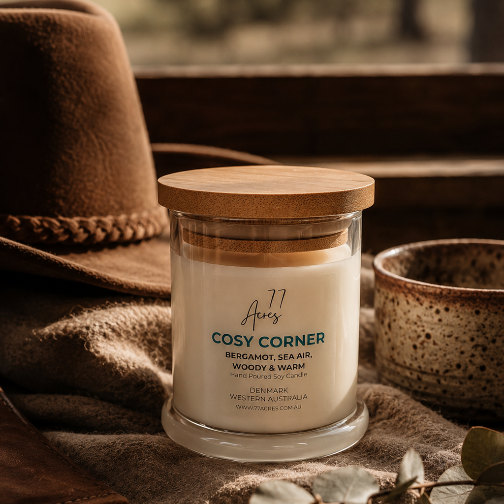 A candle named Cosy Corner positioned near a country hat with a view of a country landscape 